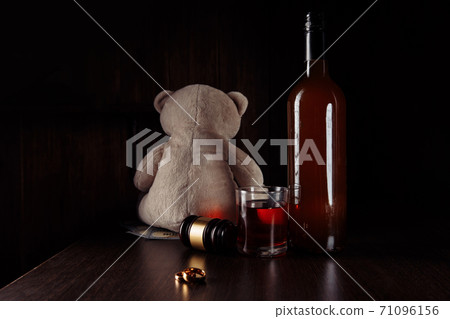 Alcohol and divorce concept. Teddy bear, rings and bottle with glass in a dark room 71096156