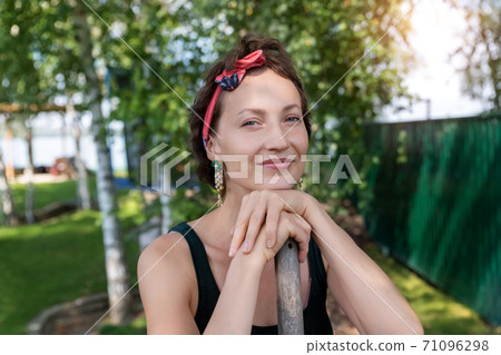 Portrait of young adult beautiful caucasian woman standing in home yard garden holding shovel or rake. Attractive female gardener agriculture worker at farming or landscaping at backyard farm 71096298