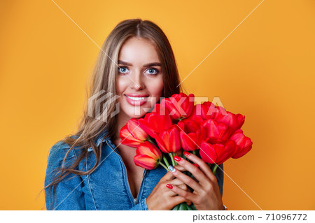 Pretty woman holding big bunch of red tulips in hands on yellow background Pretty woman holding big bunch of red tulips in hands on yellow background 71096772