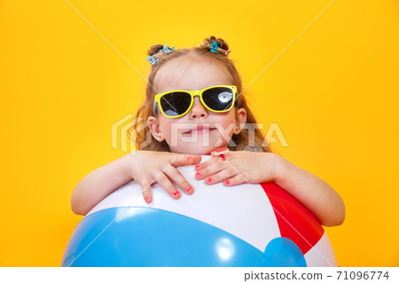 Summer girl wearing sunglasses with ball laughing on yellow background 71096774