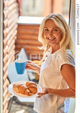 Middle aged caucasian woman holding croissants and coffee Middle aged caucasian woman holding croissants and coffee 71099227