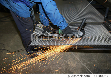 A worker cuts an iron mesh netting with an iron circle. Sparks fly 71100057
