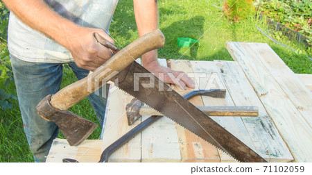 man uses a hacksaw, a hatchet, a claw hammer for construction work in your garden man uses a hacksaw, a hatchet, a claw hammer for construction work in your garden 71102059