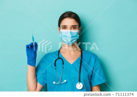 Concept of covid-19 and quarantine concept. Close-up of beautiful female doctor in medical mask, rubber gloves and scrubs, ready to vaccinate patient, holding syringe with coronavirus vaccine Concept of covid-19 and quarantine concept. Close-up of beautiful female doctor in medical mask, rubber gloves and scrubs, ready to vaccinate patient, holding syringe with coronavirus vaccine 71111374
