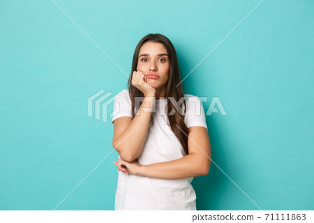 Sad and gloomy woman in white t-shirt, looking thoughtful into distance, standing over blue background Sad and gloomy woman in white t-shirt, looking thoughtful into distance, standing over blue background 71111863