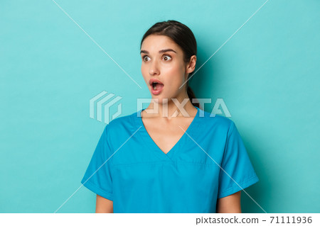 Coronavirus, social distancing and health concept. Close-up of impressed female doctor in scrubs, looking left at copy space and drop jaw amazed, standing over blue background Coronavirus, social distancing and health concept. Close-up of impressed female doctor in scrubs, looking left at copy space and drop jaw amazed, standing over blue background 71111936