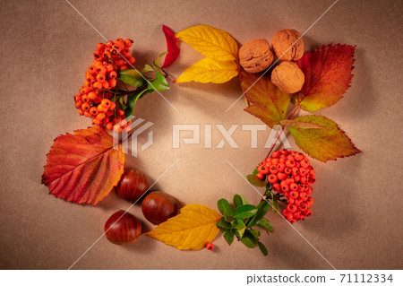 Autumn wreath with chestnuts and autumn leaves, shot from above with copy space on a brown background 71112334