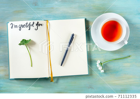 Open gratitude journal with a pen and a cup of tea, with the handwritten phrase I am grateful for Open gratitude journal with a pen and a cup of tea, with the handwritten phrase I am grateful for 71112335