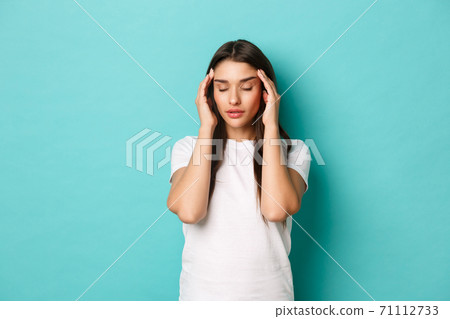Image of young attractive woman having severe headache, touching head with eyes closed, standing over blue background Image of young attractive woman having severe headache, touching head with eyes closed, standing over blue background 71112733