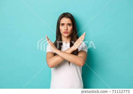 Concerned woman in white t-shirt prohibit something bad, showing cross gesture and frowning displeased, tell to stop, standing over blue background Concerned woman in white t-shirt prohibit something bad, showing cross gesture and frowning displeased, tell to stop, standing over blue background 71112773