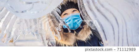 beautiful smiling young woman wearing a medical mask during COVID-19 coronavirus among the ice in wintertime outdoor. Winter concept BANNER, LONG FORMAT 71112989