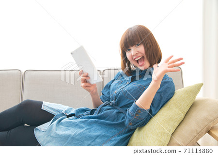 A young woman using a tablet while relaxing on the sofa at home 71113880