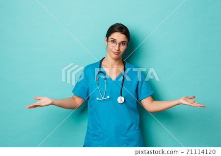 Coronavirus, pandemic and social distancing concept. Image of beautiful female doctor in glasses, scrubs and stethoscope, spread hands sideways and clueless, blue background Coronavirus, pandemic and social distancing concept. Image of beautiful female doctor in glasses, scrubs and stethoscope, spread hands sideways and clueless, blue background 71114120
