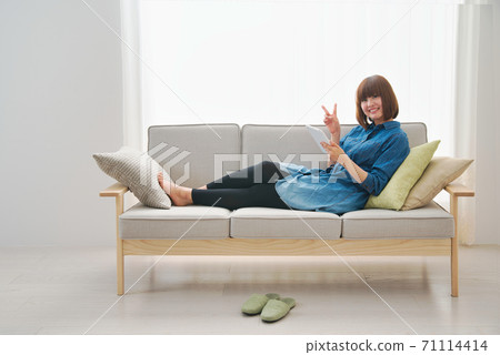 A young woman spending her time at home on a tablet while relaxing on the sofa A young woman spending her time at home on a tablet while relaxing on the sofa 71114414