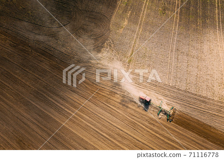 Aerial View. Tractor Plowing Field. Beginning Of Agricultural Spring Season. Cultivator Pulled By A Tractor In Countryside Rural Field Landscape. Dust Rises From Under Plows Aerial View. Tractor Plowing Field. Beginning Of Agricultural Spring Season. Cultivator Pulled By A Tractor In Countryside Rural Field Landscape. Dust Rises From Under Plows 71116778