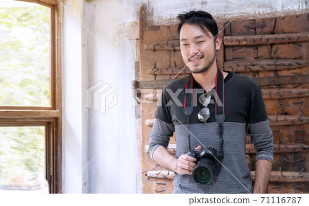 Handsome young male photographer holding digital camera and smiling to camera while standing 71116787