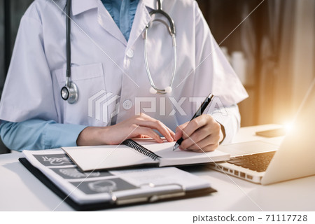 Medical students write in a notebook and work on their laptop computers at their desks during the day. Medical students write in a notebook and work on their laptop computers at their desks during the day. 71117728