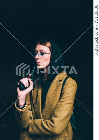 pretty young girl in olive long coat, hooded sweatshirt. Portrait of woman with hood on dark background pretty young girl in olive long coat, hooded sweatshirt. Portrait of woman with hood on dark background 71119630