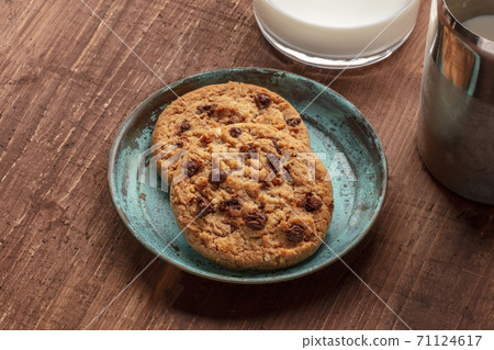 A closeup photo of chocolate chip cookies with milk on a dark rustic wooden background 71124617