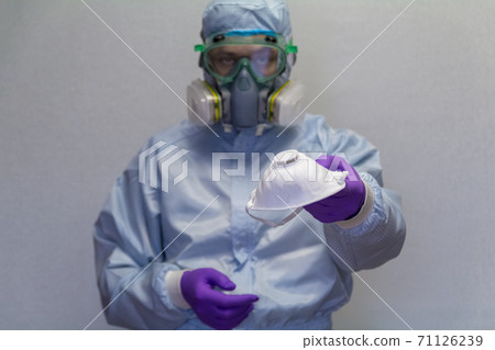 A man in a protective suit demonstrates and offers a medical mask for personal protection against viruses - health and medicine concept. A man in a protective suit demonstrates and offers a medical mask for personal protection against viruses - health and medicine concept. 71126239