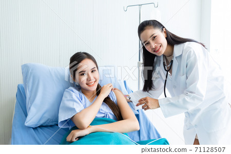 Asian young female doctor with syringe to the arm of Asian young female patient on Bed for better healing In the room hospital background. 71128507