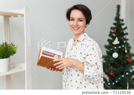 Christmas, holidays and people concept - happy young woman reading book at home. 71128536
