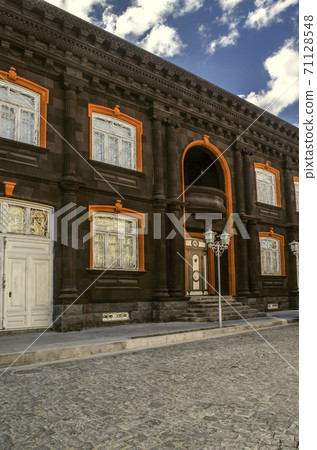 Side view of a house made of black tuff with columns and carved cornice decorated with red stone with white bars and a balcony above the main entrance 71128548