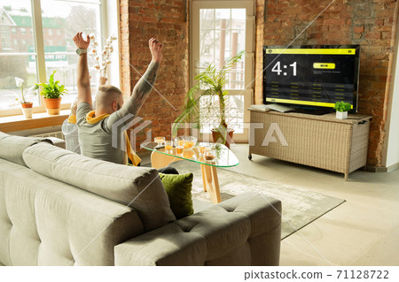 TV screen with mobile app for betting and score, cheering friends, fans in front of it look excited 71128722