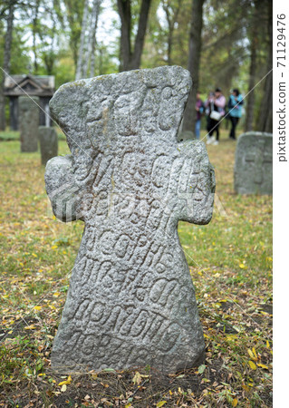 A worn sandstone grave marker in the shade on a very bright day. There is no text visible on the stone, but there is some moss on the top. Tombstone and graves in an ancient church graveyard. toned 71129476