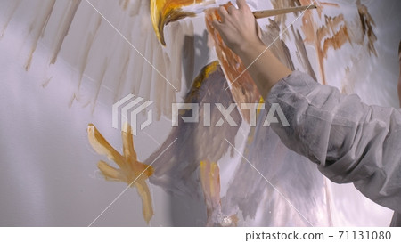 Artist designer draws an eagle on the wall. Craftsman decorator paints picture with acrylic oil color. Painter painter dressed in paint coat. Indoor. Artist designer draws an eagle on the wall. Craftsman decorator paints picture with acrylic oil color. Painter painter dressed in paint coat. Indoor. 71131080