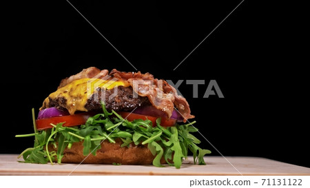 Craft burger is cooking on black background. Consist: sauce, arugula, tomato, onion, bacon, currant sauce, ricotta cheese, air bun and marble meat. 71131122