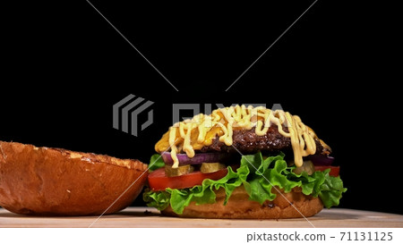 Craft burger is cooking on black background. Consist: sauce, lettuce, tomato, red onion, pickle, cheese, bacon, air bun and marbled meat beef. Craft burger is cooking on black background. Consist: sauce, lettuce, tomato, red onion, pickle, cheese, bacon, air bun and marbled meat beef. 71131125
