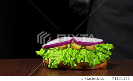 Craft burger is cooking on black background. Consist: sauce salsa, lettuce, red onion, pickle, cheese, chilli green pepper, bun, marbled meat beef. Craft burger is cooking on black background. Consist: sauce salsa, lettuce, red onion, pickle, cheese, chilli green pepper, bun, marbled meat beef. 71131165