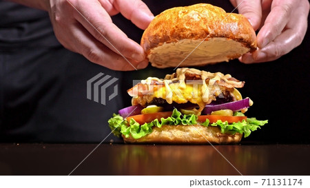Craft burger is cooking on black background. Consist: sauce, lettuce, tomato, red onion, pickle, cheese, bacon, air bun and marbled meat beef. 71131174
