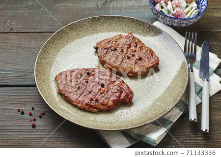 Two grilled ribeye steaks, spices and tomato-cucumber salad with sour cream Two grilled ribeye steaks, spices and tomato-cucumber salad with sour cream 71133336