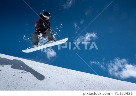 Young woman on a snowboard makes a flight after jumping from a snowy ledge against a dark blue sky high in the mountains in winter 71133421