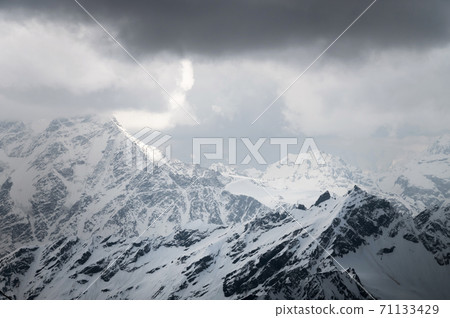 Snow-capped peaks of the Caucasian high mountains in the evening. Dramatic sky 71133429