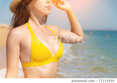 Chest, chin and body of an attractive Caucasian young woman in a yellow swimsuit against the backdrop of the azure sea and blue sky on a sunny summer day. Background for tourism and visiting the coast 71133438