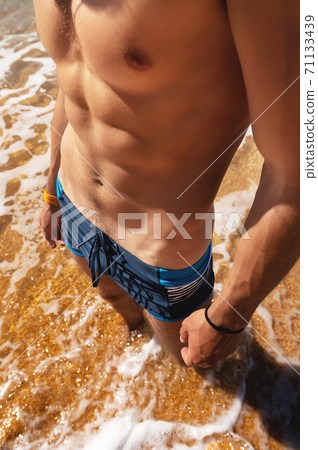 sexy naked tanned torso muscle press press unknown man on golden beach stands in water with waves and foam 71133439