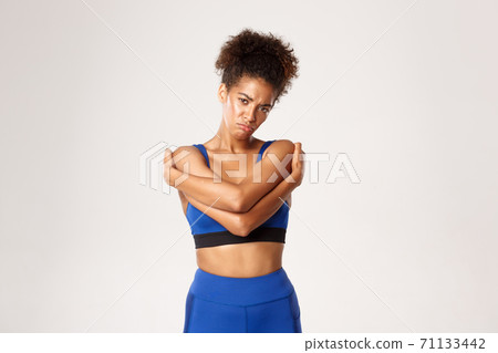 Concept of sport and workout. Sad and gloomy african-american female athlete in sportswear, hugging herself and sulking upset, feeling disappointed, white background 71133442