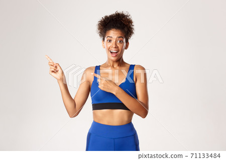 Healthy attractive sportswoman in blue sport outfit, pointing fingers left and looking surprised, showing brand name or logo, white background Healthy attractive sportswoman in blue sport outfit, pointing fingers left and looking surprised, showing brand name or logo, white background 71133484
