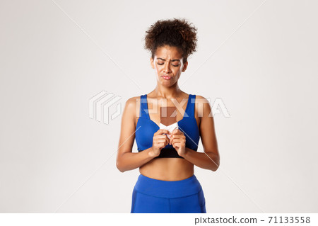 Disappointed african-american fitness woman, looking sad at chocolate bar, being on a diet, standing over white background Disappointed african-american fitness woman, looking sad at chocolate bar, being on a diet, standing over white background 71133558