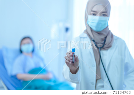 Young muslim female doctor holding test tube with blood for covid-19 analyzing with elderly patient sitting on the bed in hospital Young muslim female doctor holding test tube with blood for covid-19 analyzing with elderly patient sitting on the bed in hospital 71134763