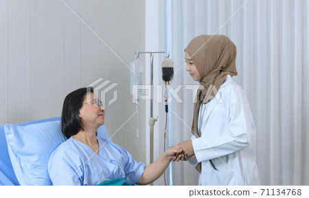 Muslim female doctor holding hand of the elderly patient sitting 71134768