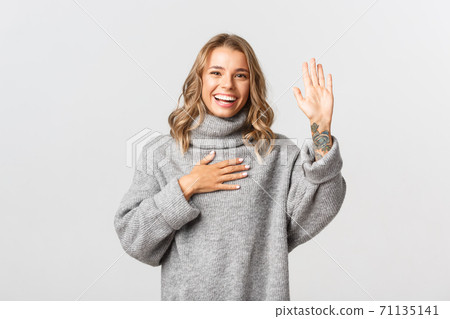 Image of happy honest girl raising one arm and put hand on heart, making promise, swear and telling truth, standing over white background Image of happy honest girl raising one arm and put hand on heart, making promise, swear and telling truth, standing over white background 71135141