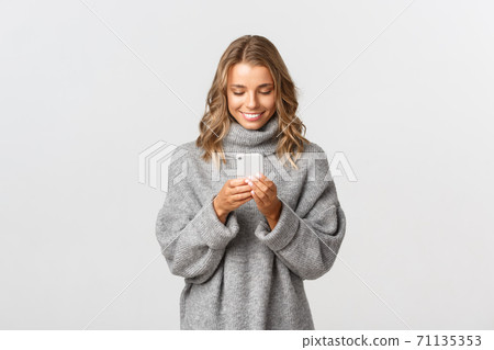 Portrait of young caucasian girl with short blond hair using mobile phone, messaging online, standing over white background Portrait of young caucasian girl with short blond hair using mobile phone, messaging online, standing over white background 71135353