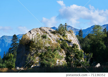 detached huge limestone cliff overgrown with trees against the backdrop of a mountain range detached huge limestone cliff overgrown with trees against the backdrop of a mountain range 71136352