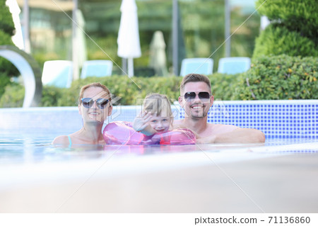 Family mom dad girl stand in pool and smile. 71136860