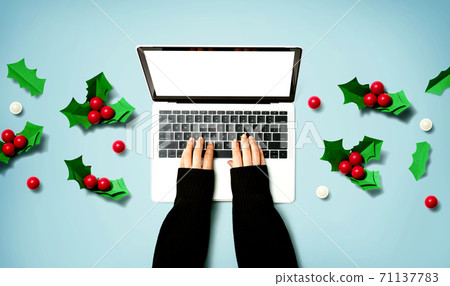 Person using a laptop computer with Christmas holly berries Person using a laptop computer with Christmas holly berries 71137783