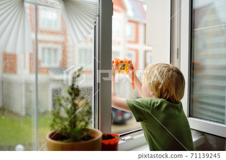 Little boy watching the rain outside at opened window and taking photo. Little boy watching the rain outside at opened window and taking photo. 71139245